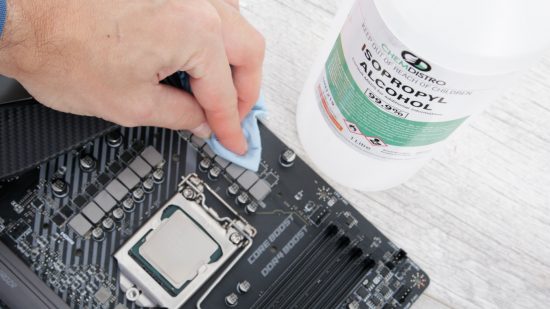 A gaming motherboard with exposed VRMs, a hand is cleaning them