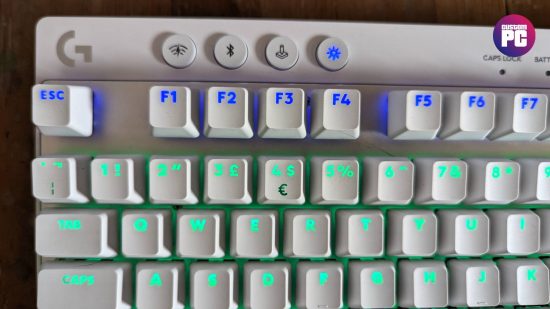 Logitech G Pro X TKL Lightspeed review: the top left of a white keyboard with blue and turquoise RGB lighting is shown above a wooden worktop.